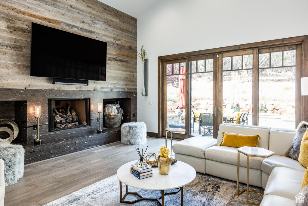 Living room featuring a fireplace, wood walls, light hardwood / wood-style floors, and a towering ceiling