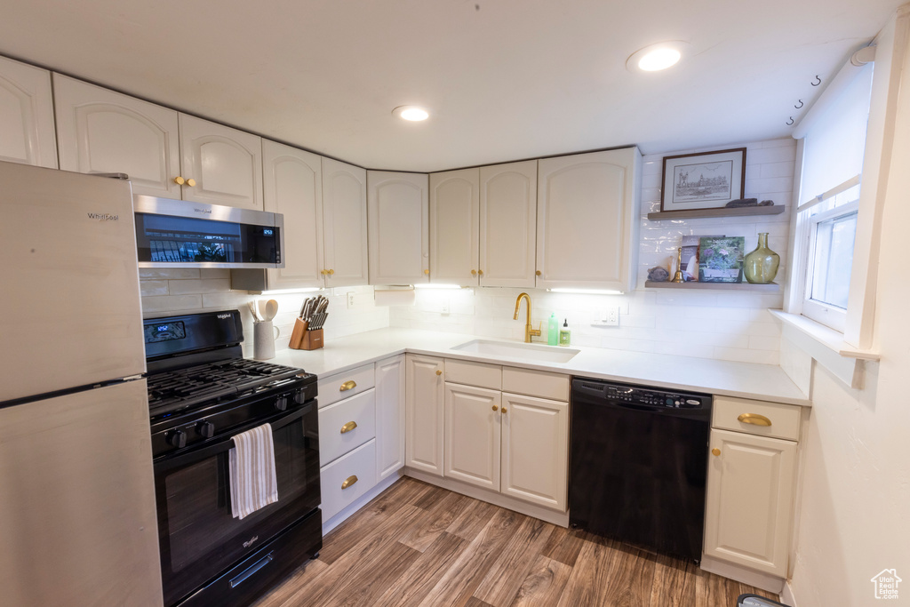 Kitchen with sink, light hardwood / wood-style flooring, black appliances, tasteful backsplash, and white cabinetry