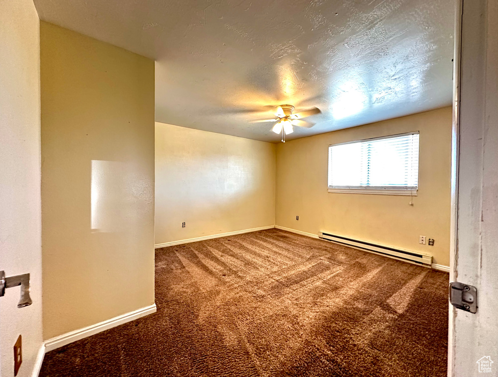Empty room with dark carpet, a baseboard heating unit, and ceiling fan