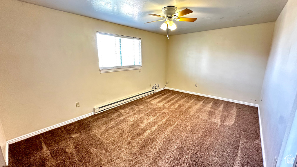 Carpeted spare room featuring a baseboard radiator and ceiling fan