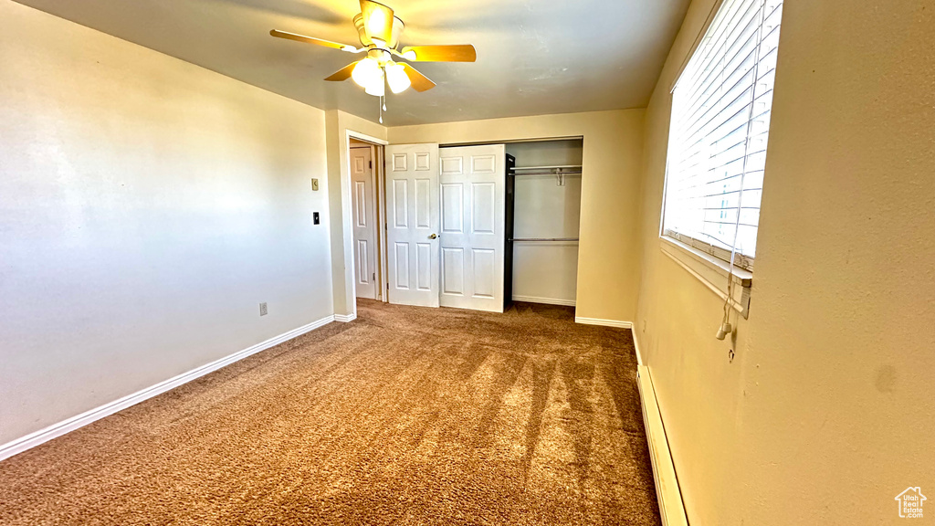 Unfurnished bedroom featuring ceiling fan, baseboard heating, dark carpet, and a closet