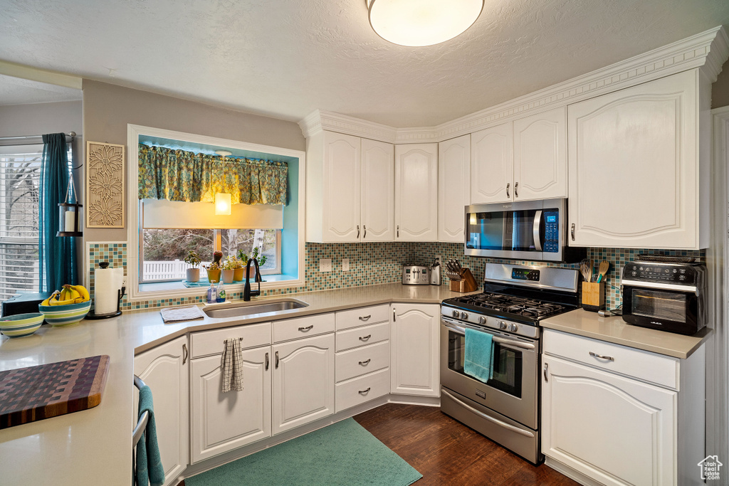 Kitchen featuring stainless steel appliances, white cabinets, sink, dark hardwood / wood-style flooring, and tasteful backsplash