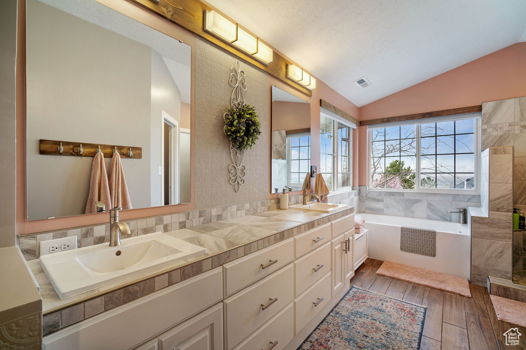 Bathroom featuring wood-type flooring, vaulted ceiling, tiled tub, and double sink vanity