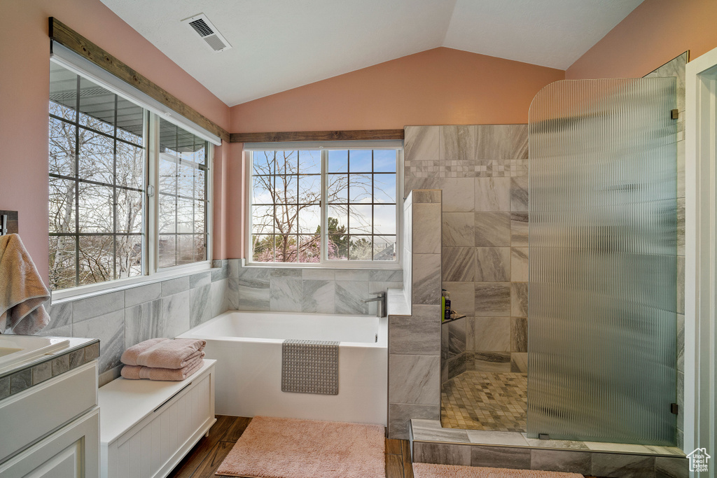 Bathroom featuring wood-type flooring, tile walls, independent shower and bath, and vaulted ceiling