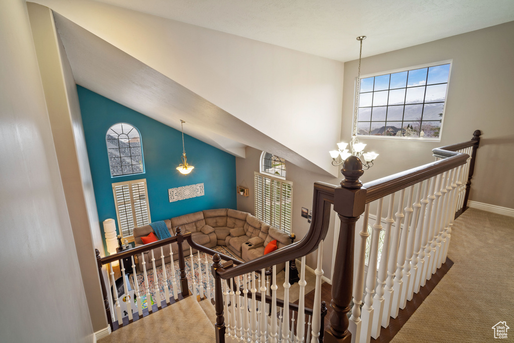 Stairway featuring high vaulted ceiling, a notable chandelier, light carpet, and plenty of natural light