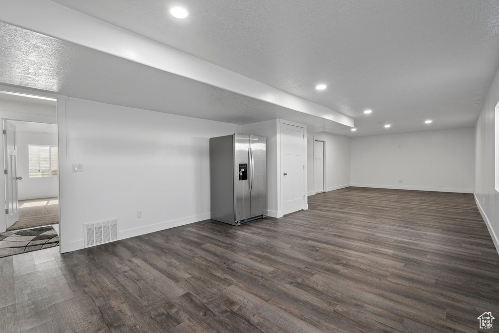 Basement with stainless steel refrigerator with ice dispenser and dark wood-type flooring