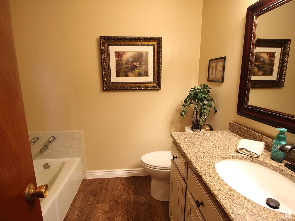 Bathroom featuring toilet, wood-type flooring, vanity with extensive cabinet space, and a bath