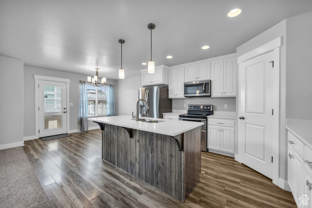 Kitchen featuring an inviting chandelier, appliances with stainless steel finishes, a kitchen island with sink, dark hardwood / wood-style floors, and decorative light fixtures