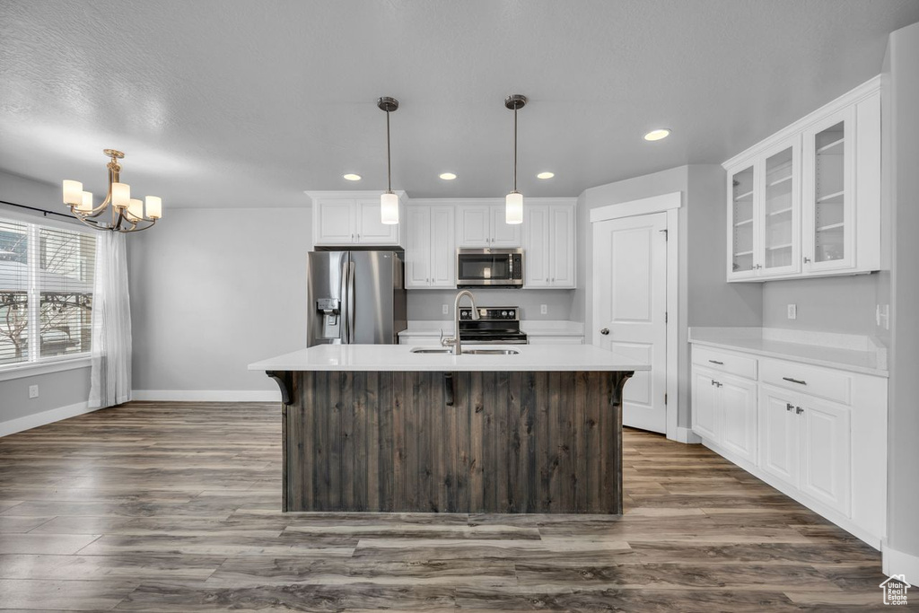 Kitchen featuring dark wood-type flooring, appliances with stainless steel finishes, a chandelier, pendant lighting, and white cabinetry