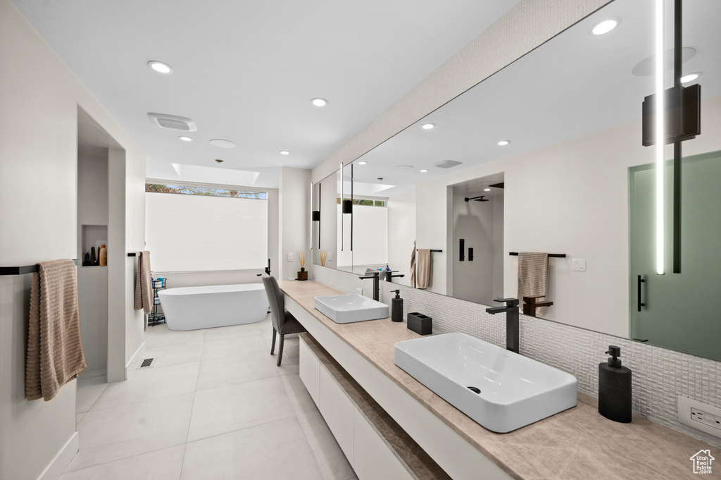 Bathroom featuring dual sinks, oversized vanity, a bath, tile walls, and tile floors