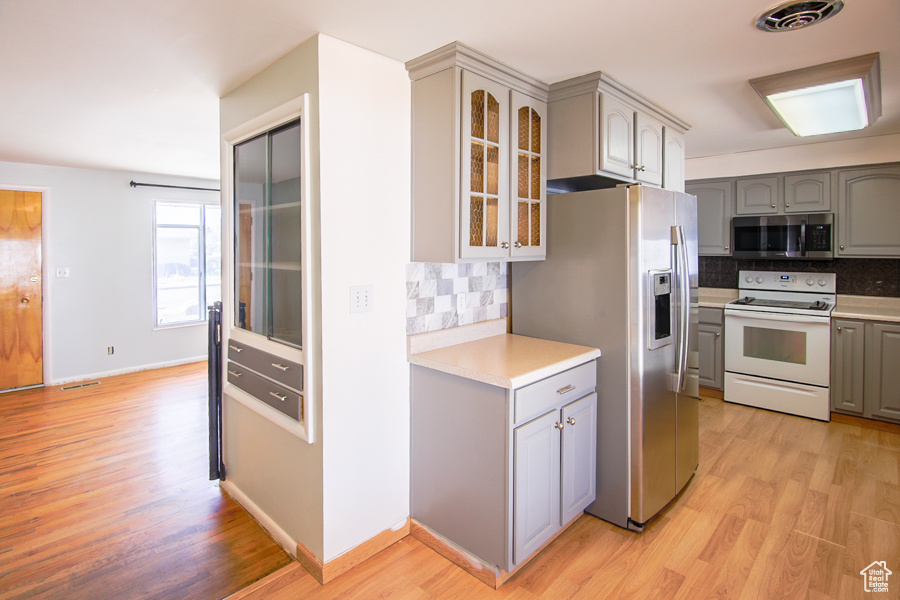 Kitchen with light hardwood / wood-style floors, tasteful backsplash, stainless steel appliances, and gray cabinets