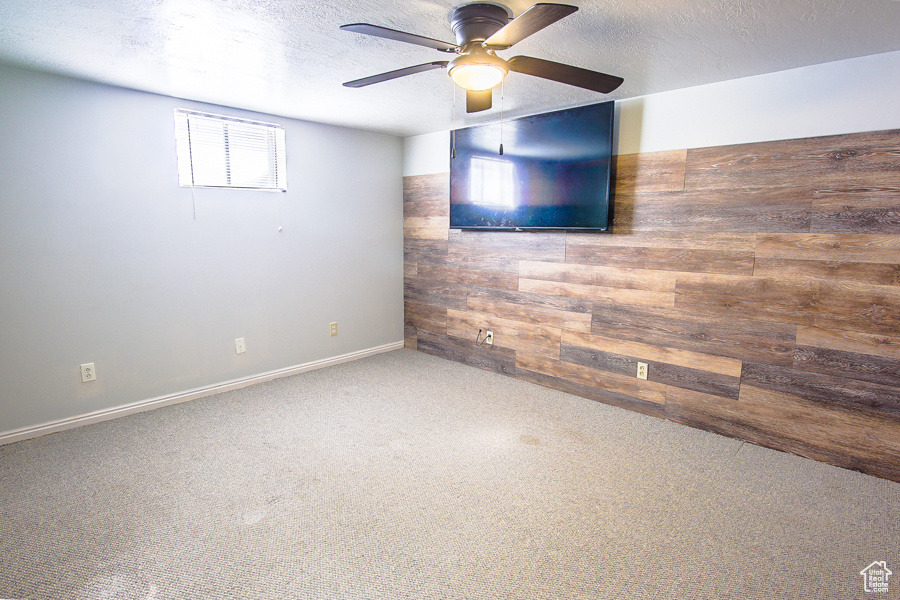 Spare room featuring wood walls, carpet, ceiling fan, and a textured ceiling