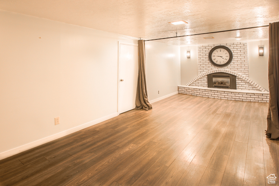 Unfurnished living room with brick wall, hardwood / wood-style flooring, a fireplace, and a textured ceiling