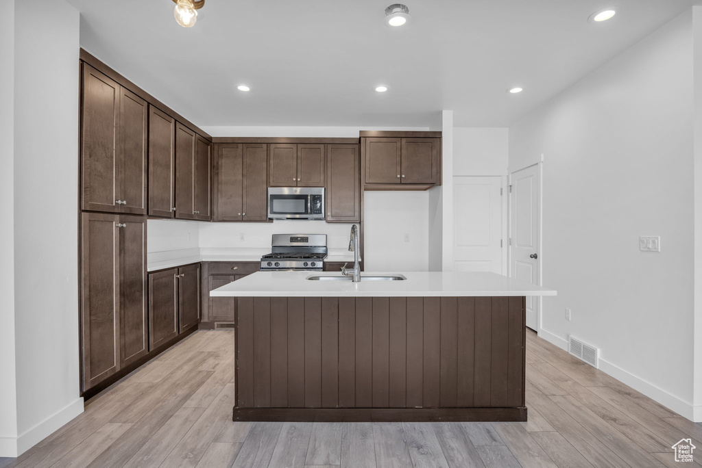 Kitchen featuring an island with sink, sink, dark brown cabinets, stainless steel appliances, and light hardwood / wood-style flooring