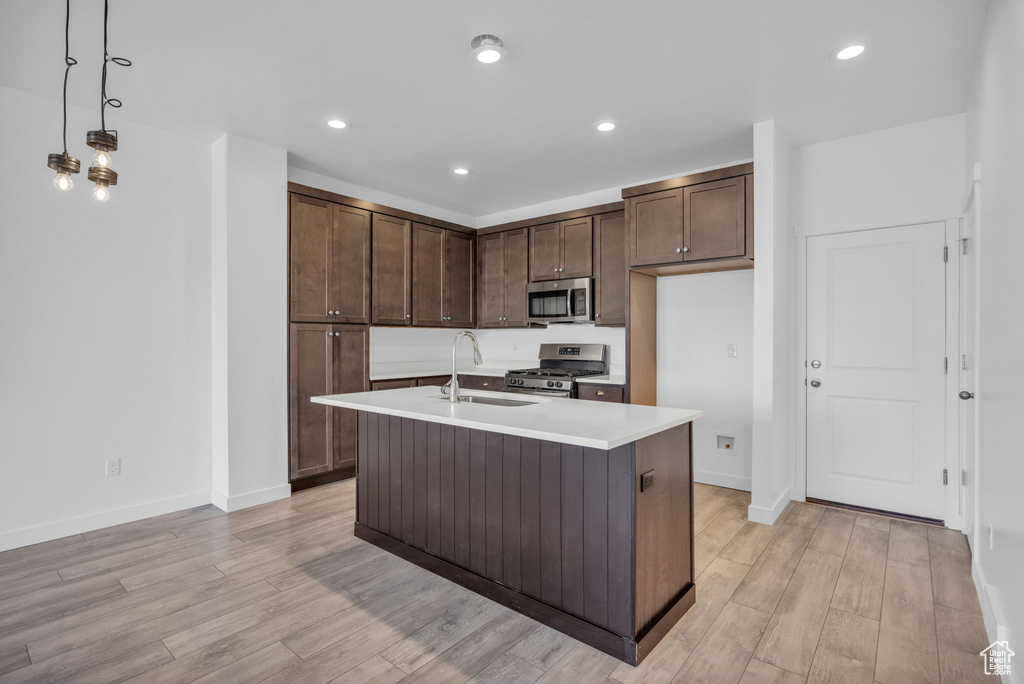 Kitchen with decorative light fixtures, a center island with sink, light hardwood / wood-style floors, and stainless steel appliances