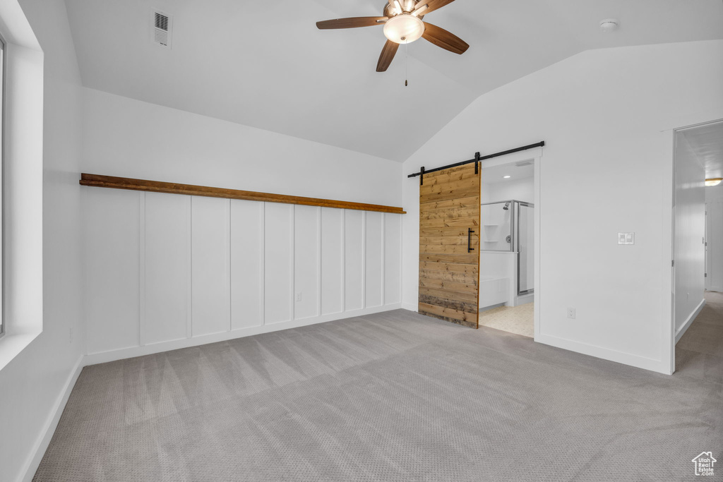 Carpeted empty room featuring a barn door, ceiling fan, and vaulted ceiling