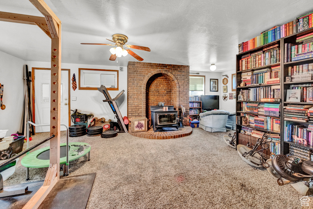 Sitting room featuring ceiling fan, a wood stove, a textured ceiling, and carpet flooring