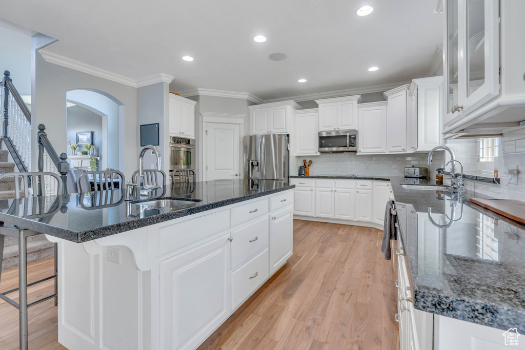 Kitchen featuring white cabinets, stainless steel appliances, sink, a center island with sink, and light hardwood / wood-style floors