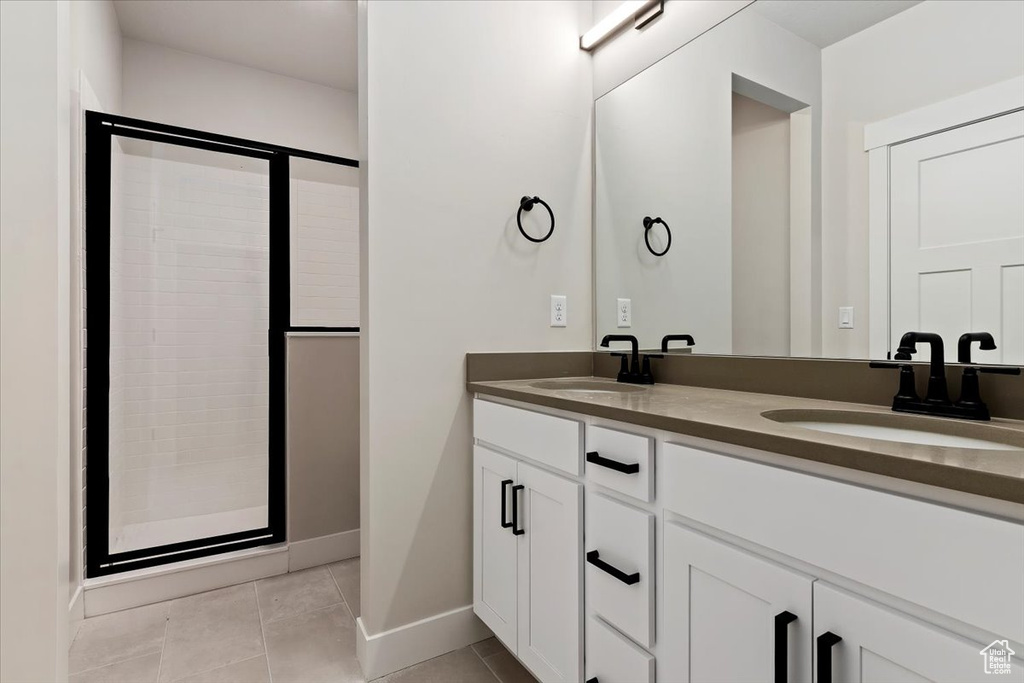 Bathroom featuring dual sinks, tile floors, oversized vanity, and a shower with shower door