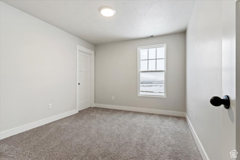 Empty room with a textured ceiling and light colored carpet