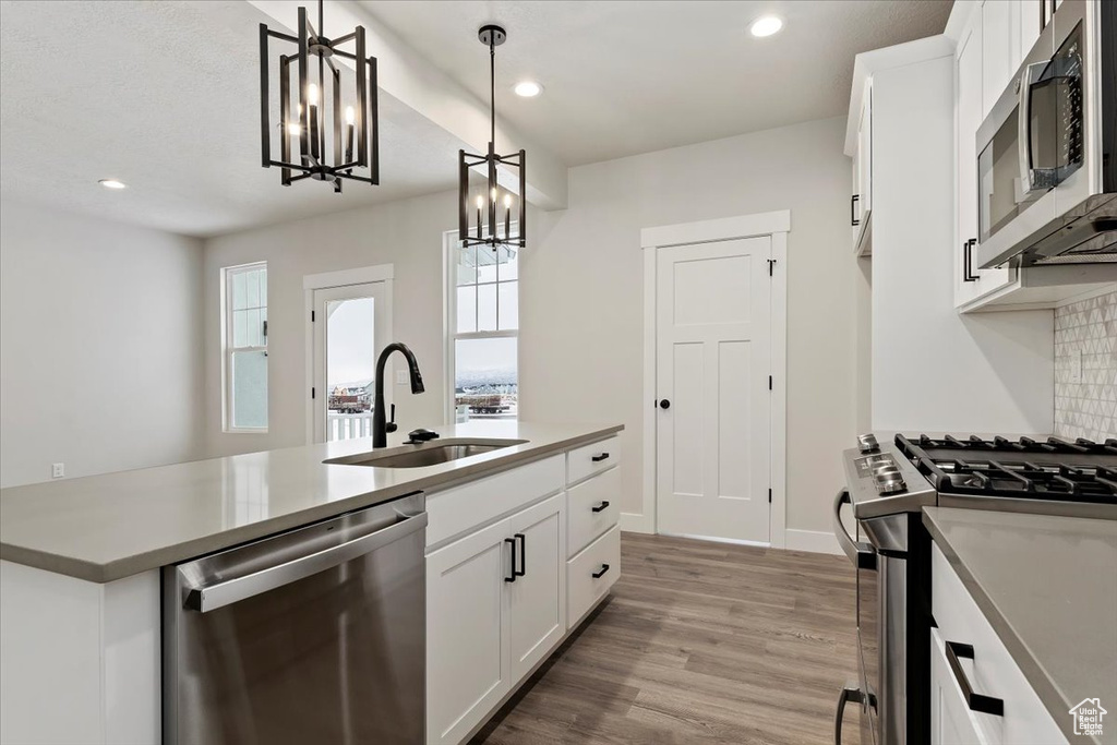 Kitchen with decorative light fixtures, white cabinetry, stainless steel appliances, hardwood / wood-style floors, and sink
