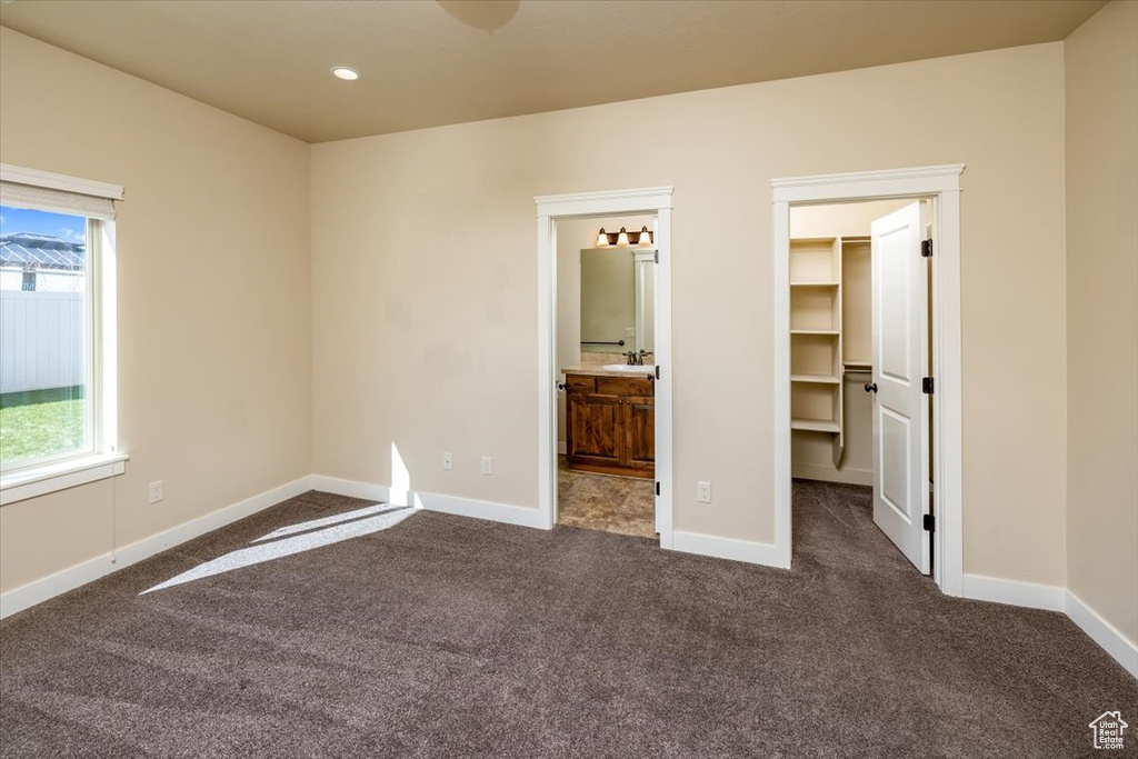 Unfurnished bedroom featuring connected bathroom, dark colored carpet, and a spacious closet