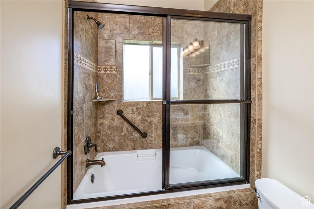 Bathroom featuring toilet and bath / shower combo with glass door