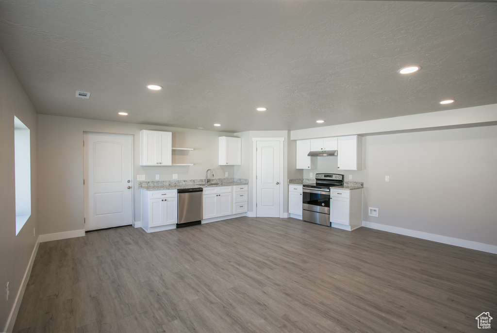 Kitchen with white cabinets, stainless steel appliances, wood-type flooring, light stone countertops, and sink