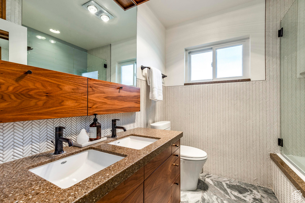 Bathroom featuring vanity with extensive cabinet space, tasteful backsplash, and toilet