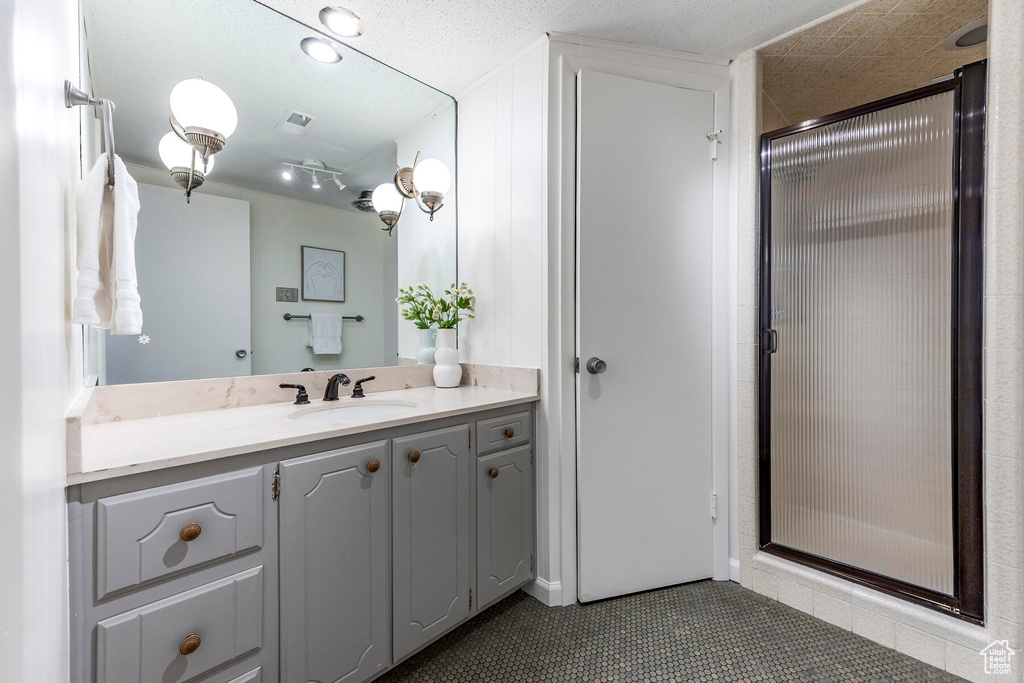 Bathroom featuring a shower with door, vanity with extensive cabinet space, a textured ceiling, and tile flooring