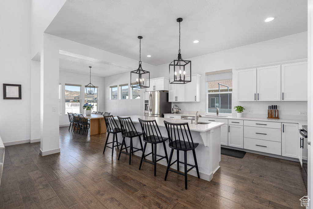 Kitchen featuring stainless steel fridge, a center island with sink, decorative light fixtures, white cabinetry, and dark hardwood / wood-style floors
