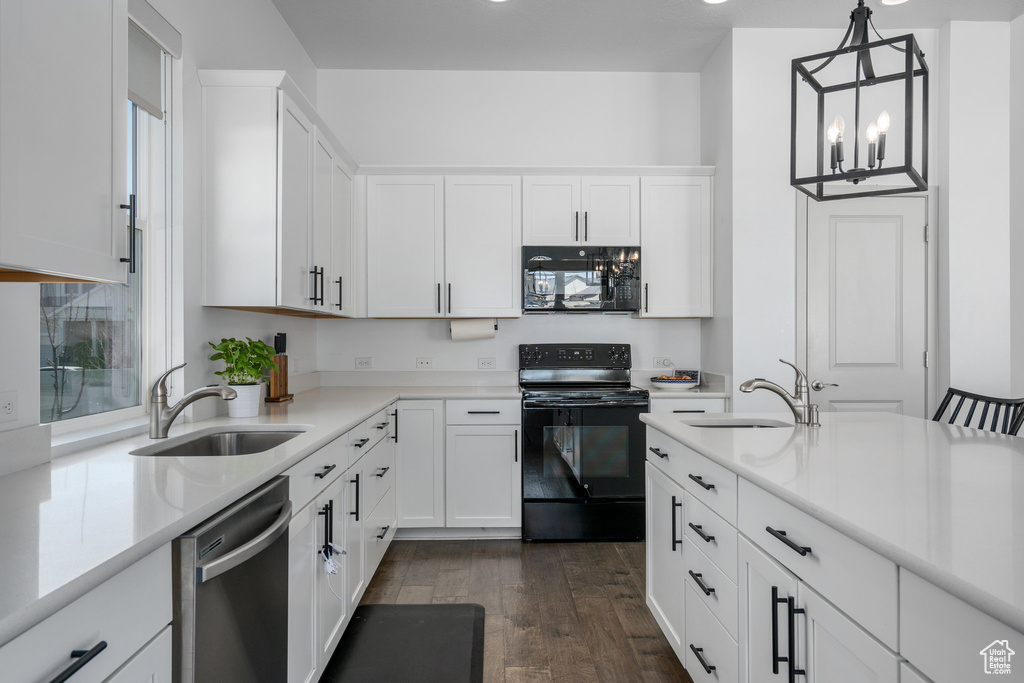 Kitchen with dark wood-type flooring, white cabinets, black appliances, and decorative light fixtures