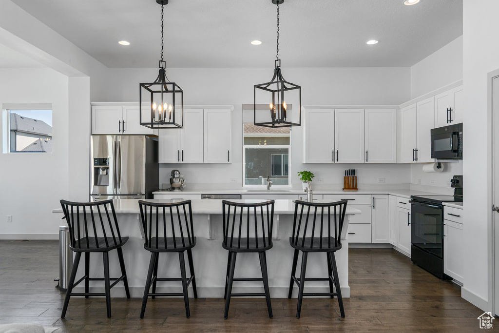 Kitchen with hanging light fixtures, dark wood-type flooring, white cabinetry, and black appliances