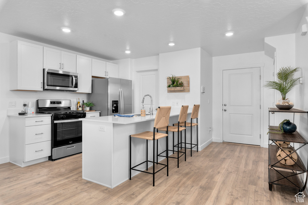 Kitchen with light hardwood / wood-style flooring, appliances with stainless steel finishes, an island with sink, and a breakfast bar