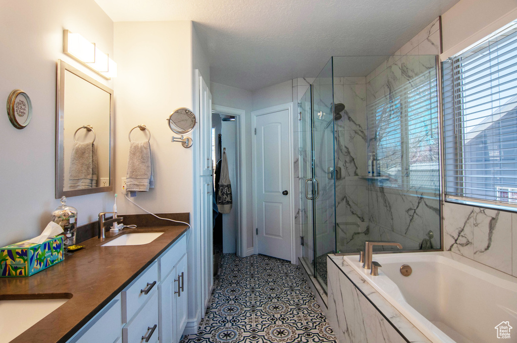 Bathroom featuring shower with separate bathtub, dual sinks, tile flooring, and vanity with extensive cabinet space