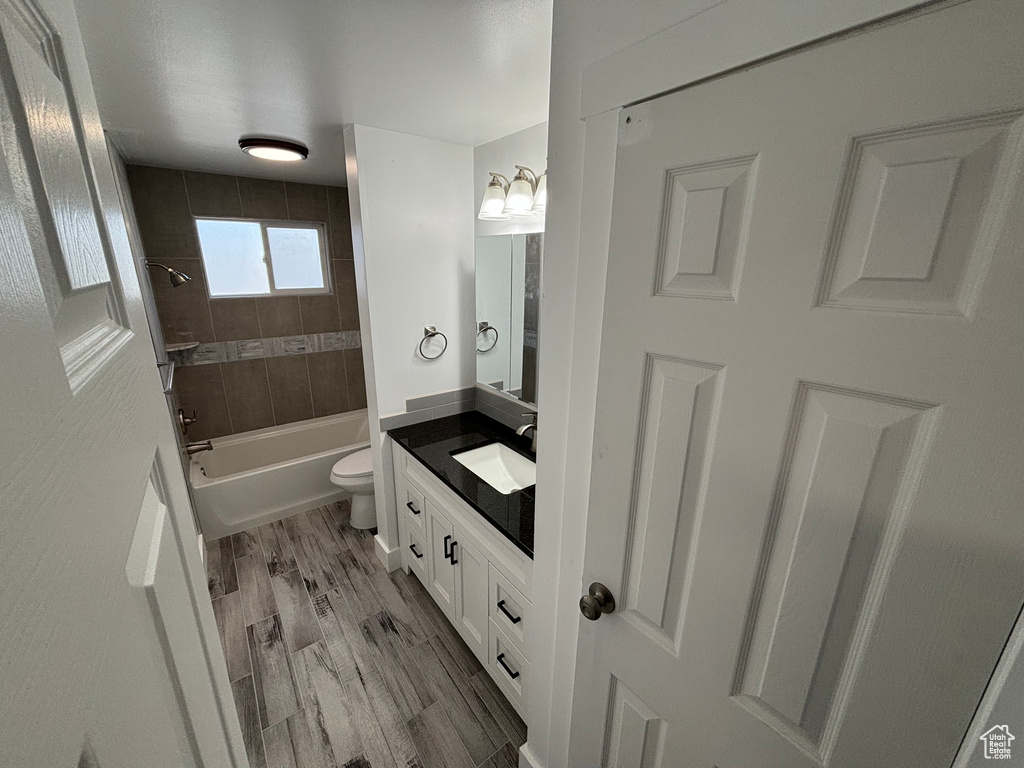 Full bathroom featuring tiled shower / bath combo, toilet, wood-type flooring, and vanity with extensive cabinet space