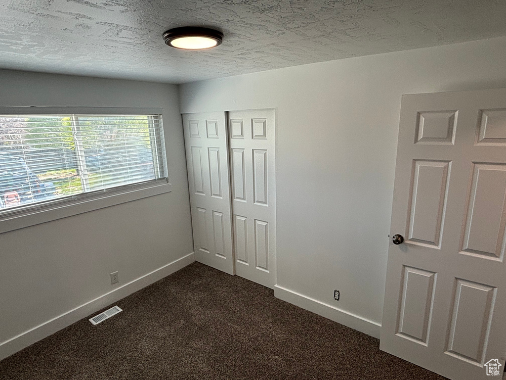 Unfurnished bedroom with a closet, dark carpet, and a textured ceiling