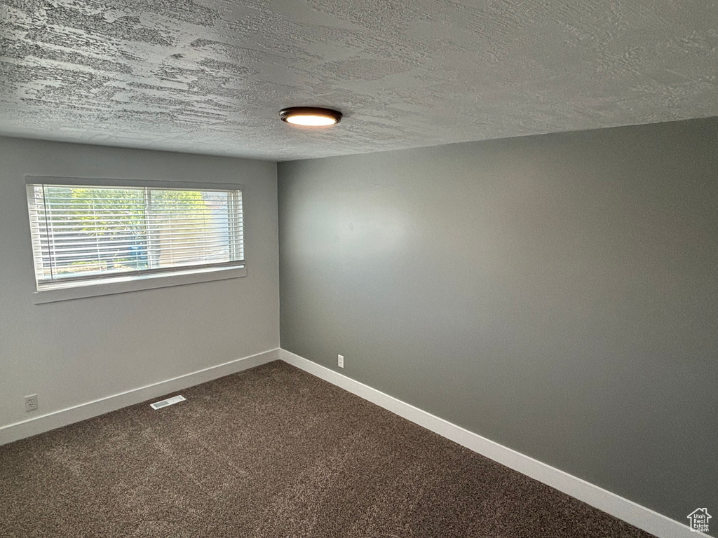 Unfurnished room featuring dark colored carpet and a textured ceiling