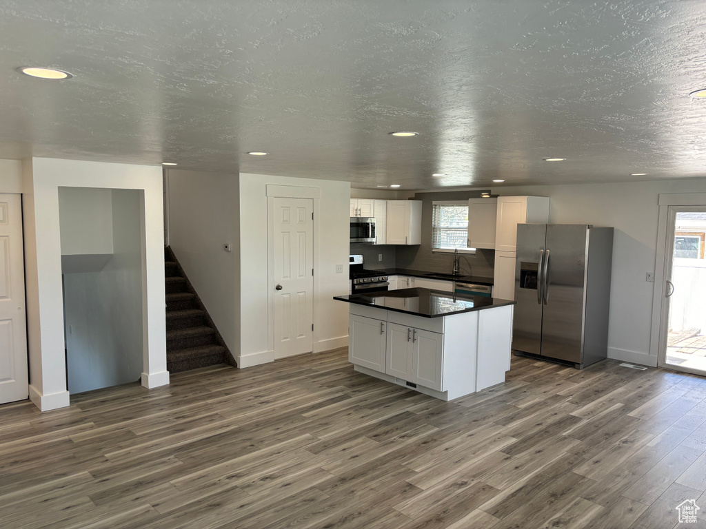 Kitchen featuring dark wood-type flooring, white cabinets, stainless steel appliances, a center island, and a textured ceiling
