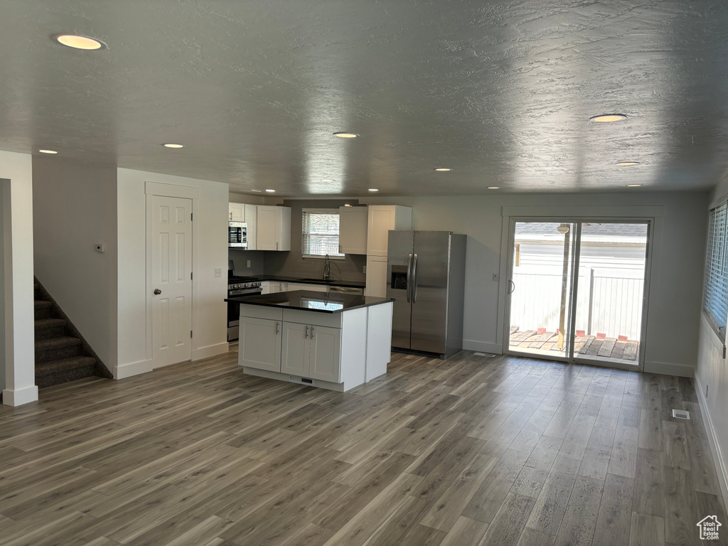 Kitchen with dark wood-type flooring, appliances with stainless steel finishes, white cabinets, a center island, and sink