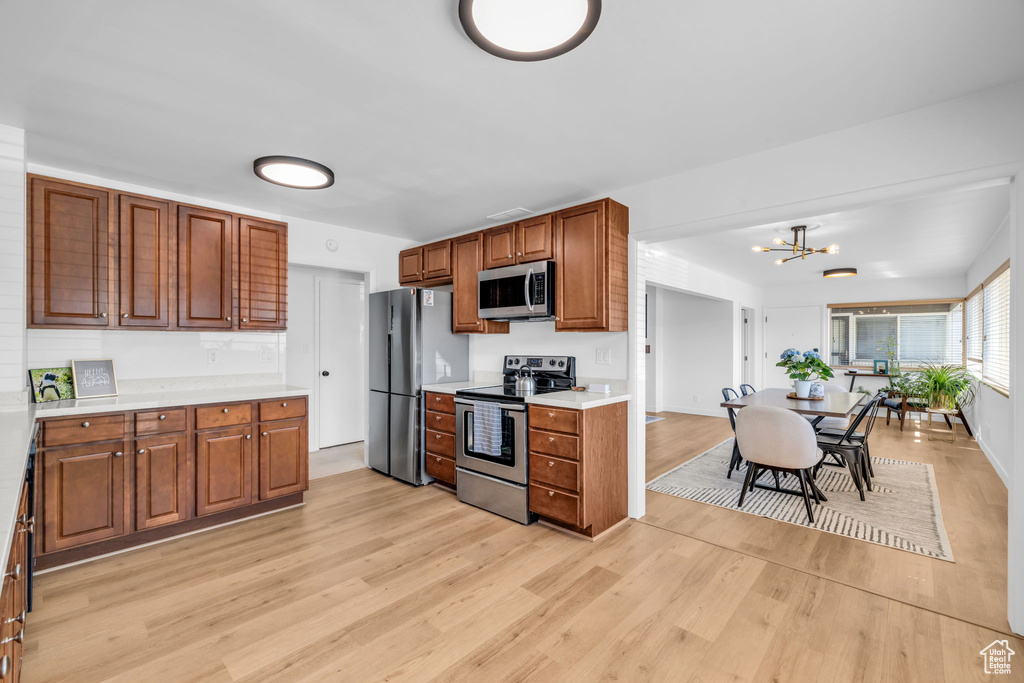Kitchen with appliances with stainless steel finishes, an inviting chandelier, and light hardwood / wood-style floors