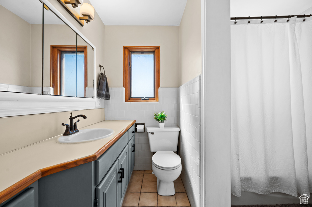 Bathroom with toilet, vanity, plenty of natural light, and tile walls