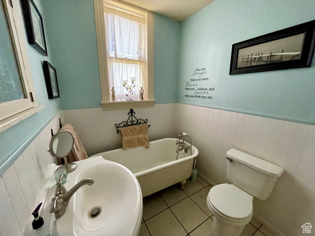 Bathroom with toilet, a bathtub, a textured ceiling, sink, and tile floors