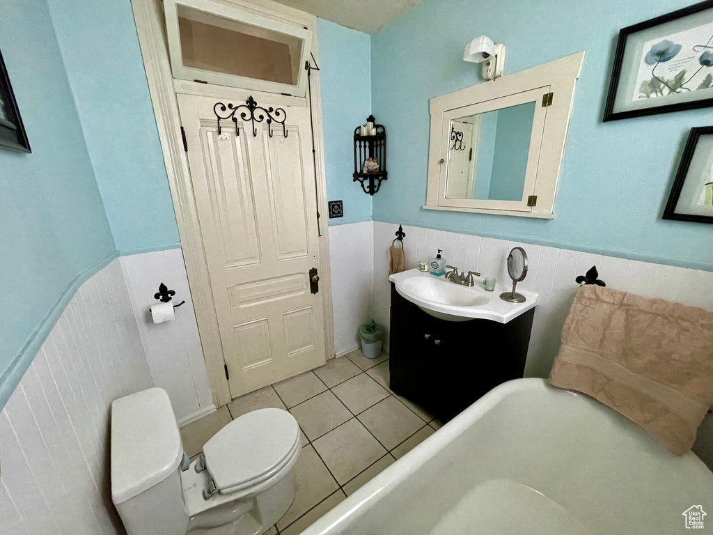 Bathroom with tile flooring, tile walls, toilet, vanity, and a washtub