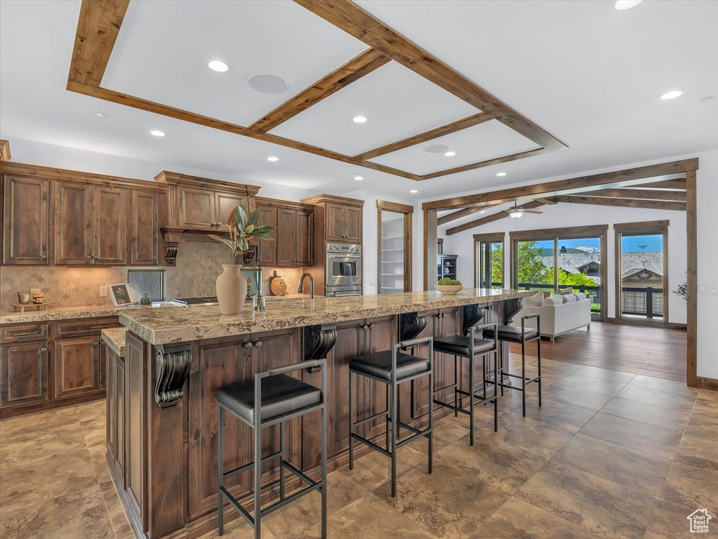 Kitchen with tasteful backsplash, a kitchen bar, a spacious island, light stone counters, and open floor plan