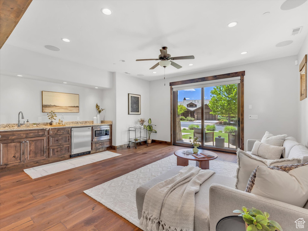 Living area with bar with sink, light wood-style flooring, ceiling fan, recessed lighting, and baseboards
