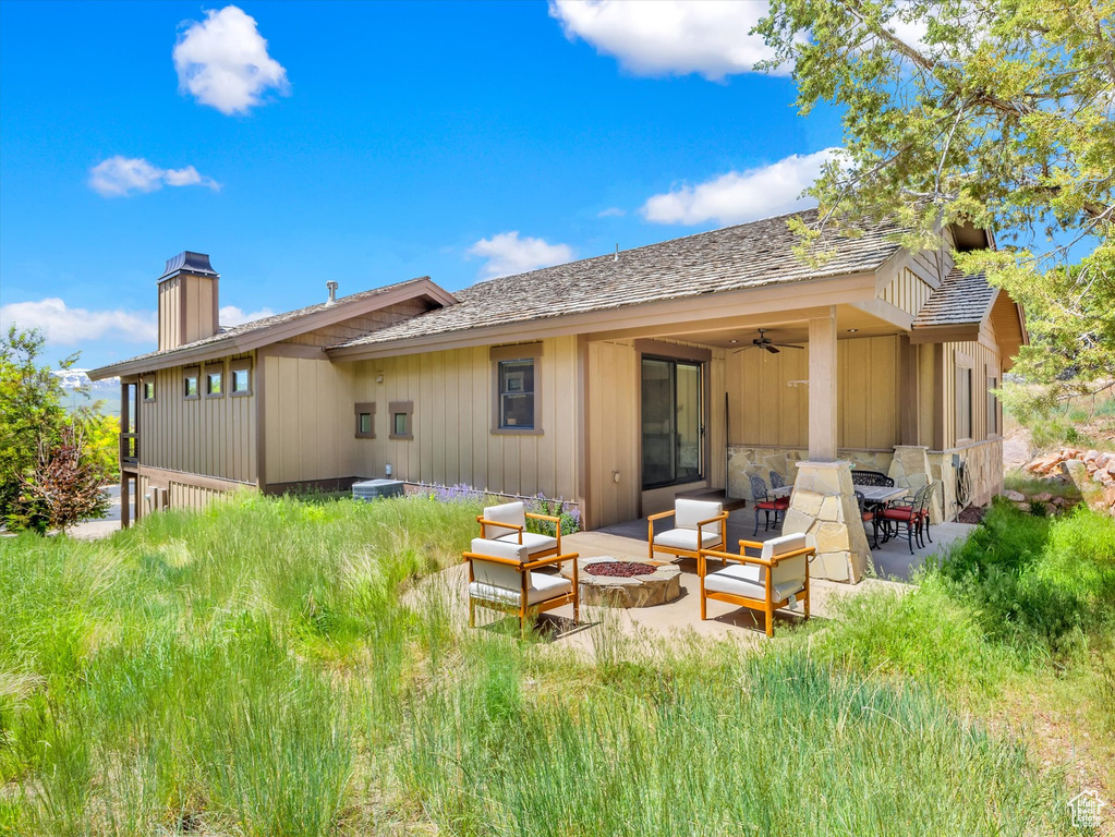 Rear view of house featuring a chimney, a patio area, a ceiling fan, and an outdoor living space with a fire pit