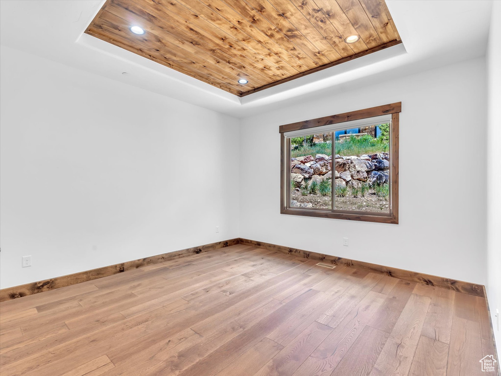 Empty room with a raised ceiling, wood ceiling, baseboards, hardwood / wood-style floors, and recessed lighting