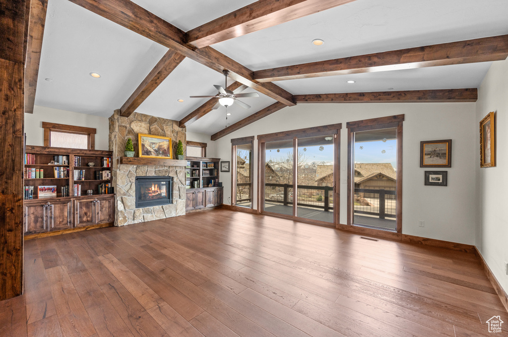 Unfurnished living room featuring ceiling fan, a stone fireplace, dark wood-type flooring, and lofted ceiling with beams