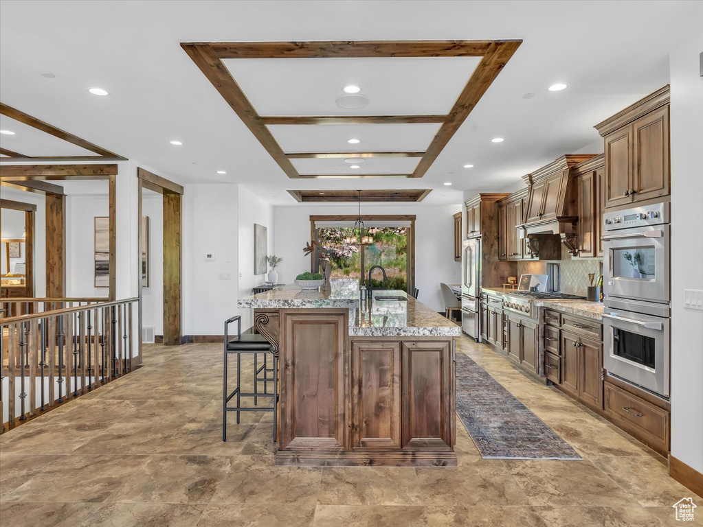 Kitchen with appliances with stainless steel finishes, an island with sink, a kitchen breakfast bar, recessed lighting, and light stone counters